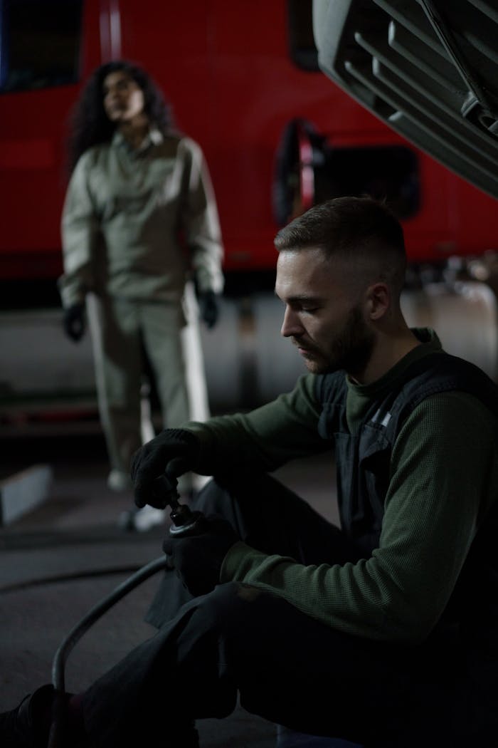 Two mechanics working on a vehicle engine inside a garage at night.
